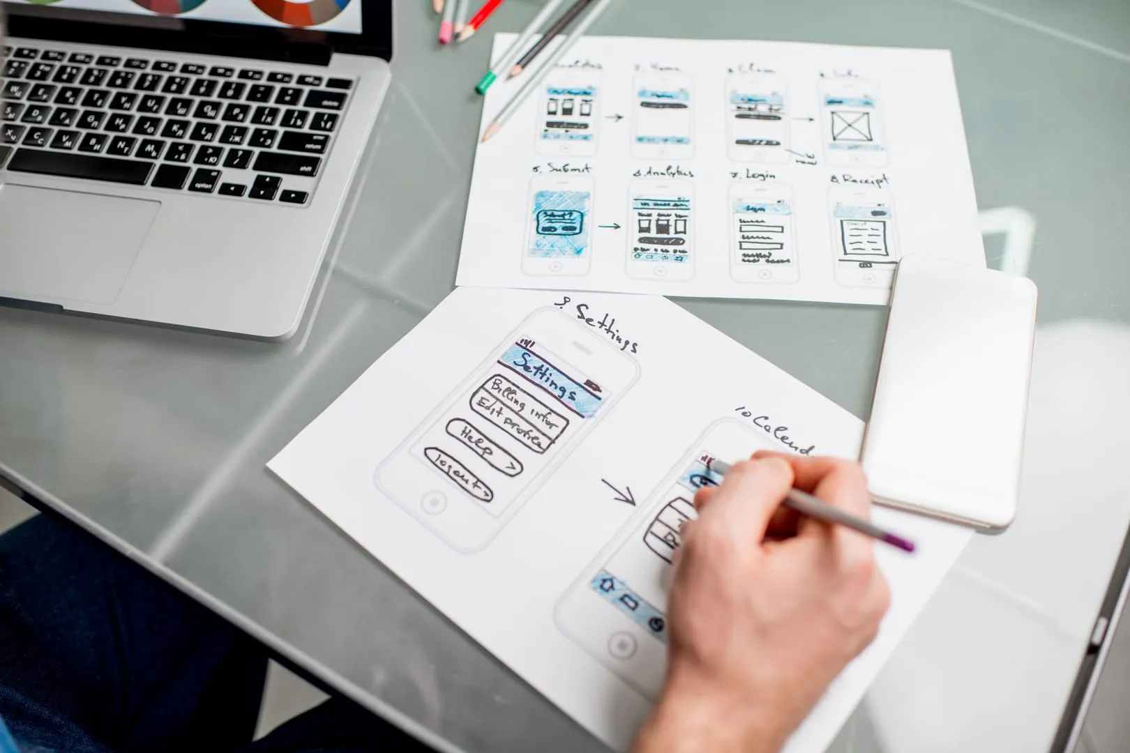 UX designer sketching mobile app wireframes and user flows on paper at a desk