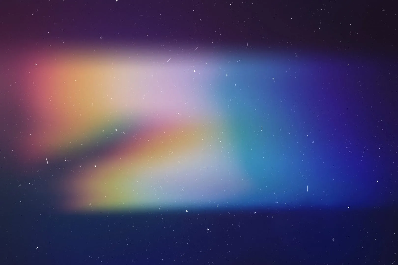 Soft pastel film light leak across a dark grainy field.
